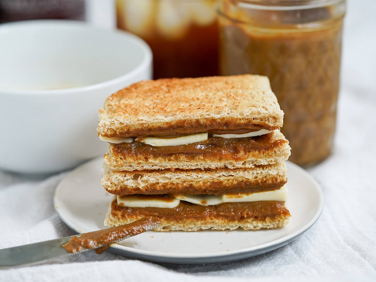 two pieces of kaya toast stacked on plate with knife resting on plate and jar behind.