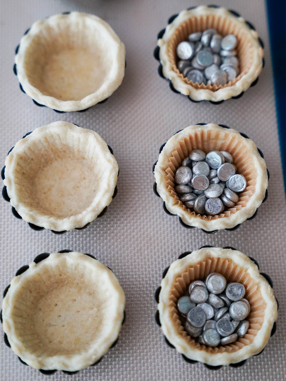 making pastry shells for strawberry tartlets part baked pastry cases, some filled with liner with baking beans inside.