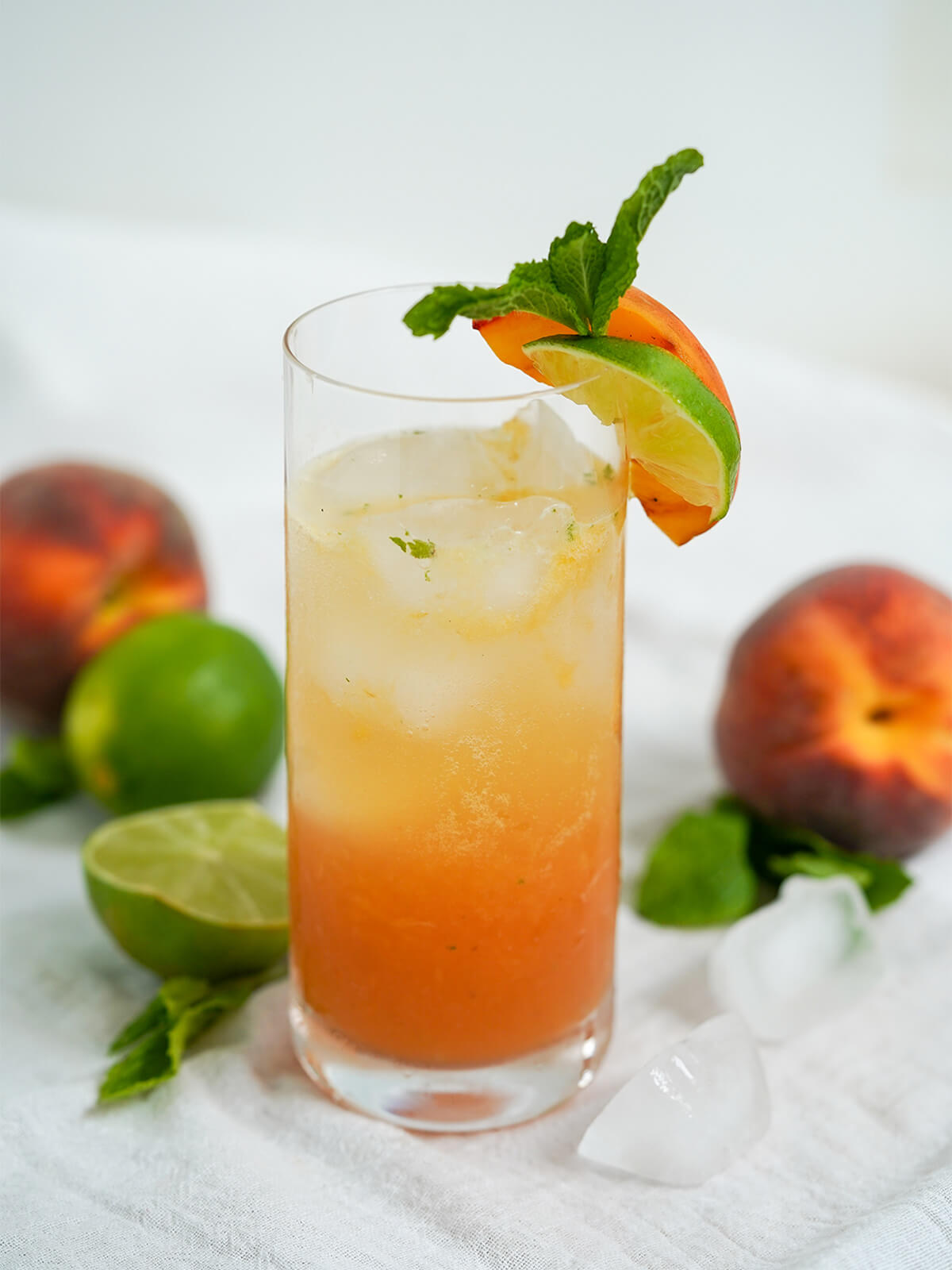 glass of peach mojito garnishes with slices of lime, peach and sprig of mint.