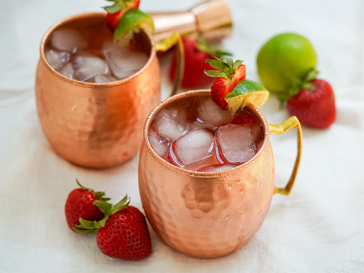 strawberry Moscow mule two copper mugs of strawberry Moscow mule with strawberries and lime to sides.