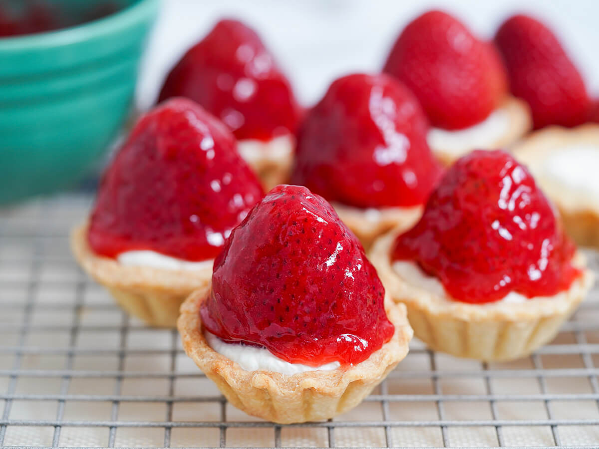 strawberry tartlets a few strawberry tartlets on rack with part of green bowl blurred in back.