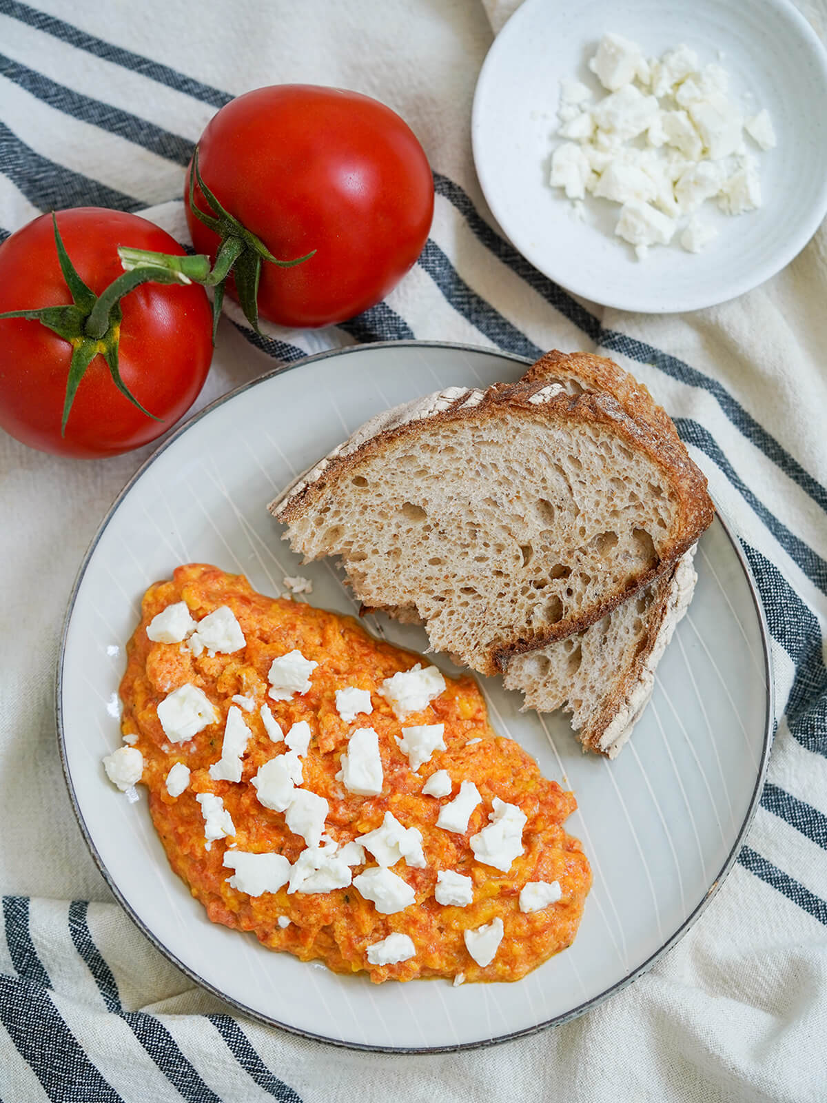 overhead view of Greek eggs with tomato strapatsada and bread on plate with tomatoes above plate.