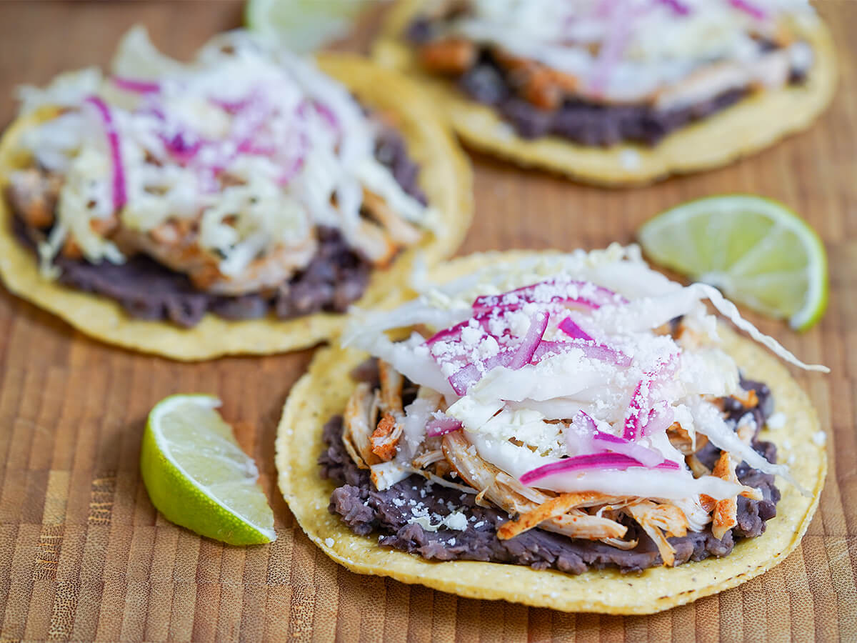 side view of three chicken tostadas in front of each other with lime wedges to side.