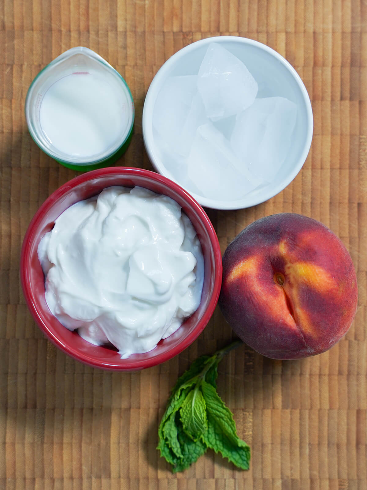 bowls with yogurt, ice, measure of milk, a peach and sprig of mint.