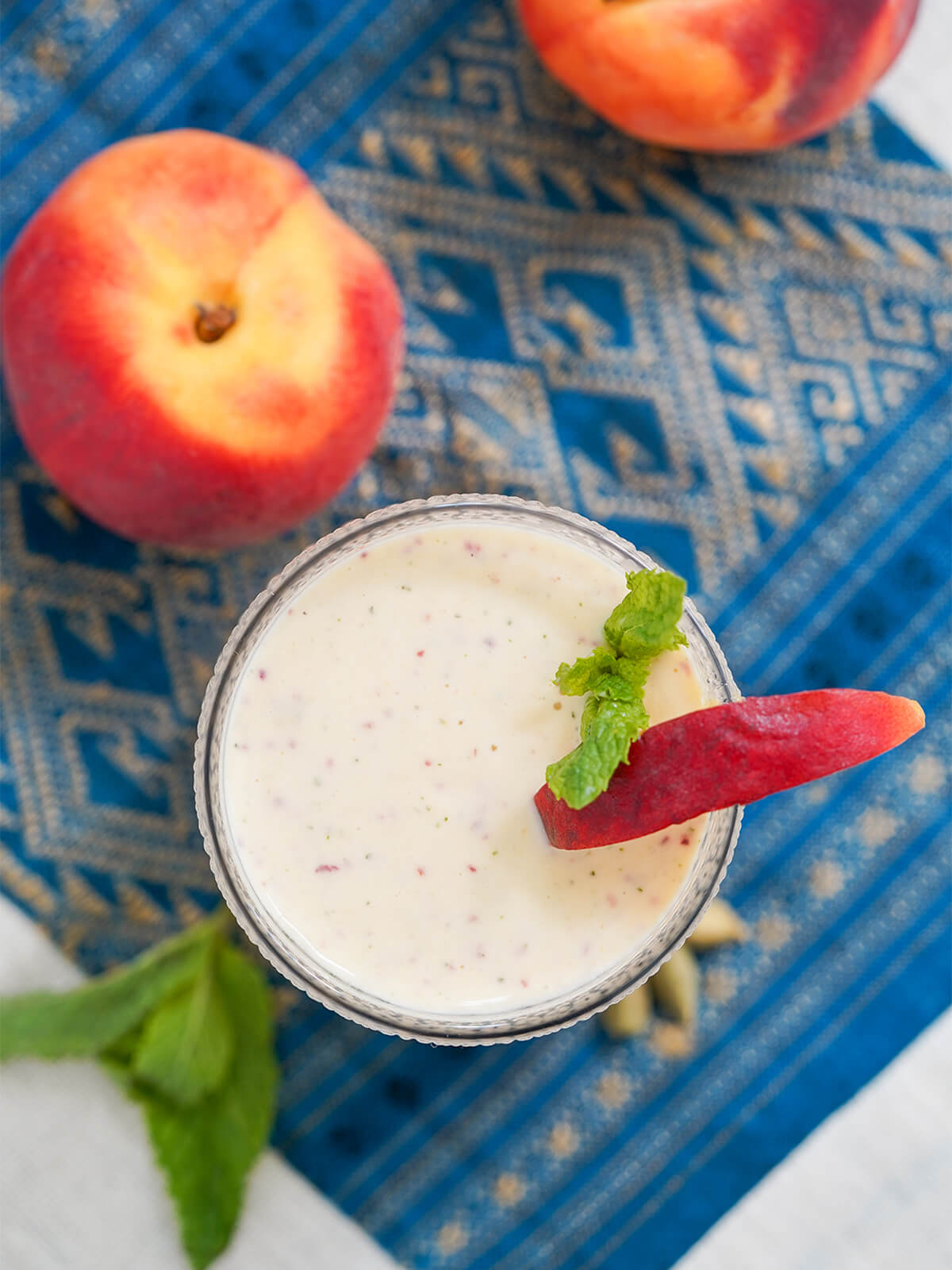overhead view of a glass with a peach slice and some mint to side in glass with peach on cloth below.