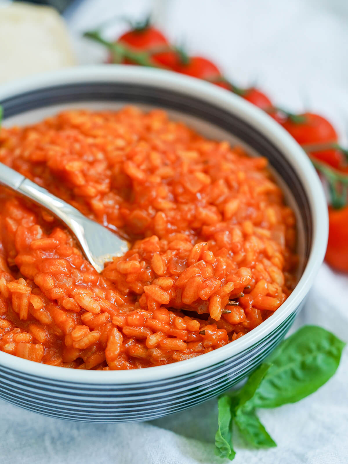 side view of bowl of tomato risotto with fork taking forkful resting on top to front.