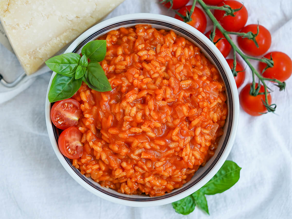 overhead view of bowl of tomato risotto with part view of bunch of tomatoes and chunk of parmesan above bowl.