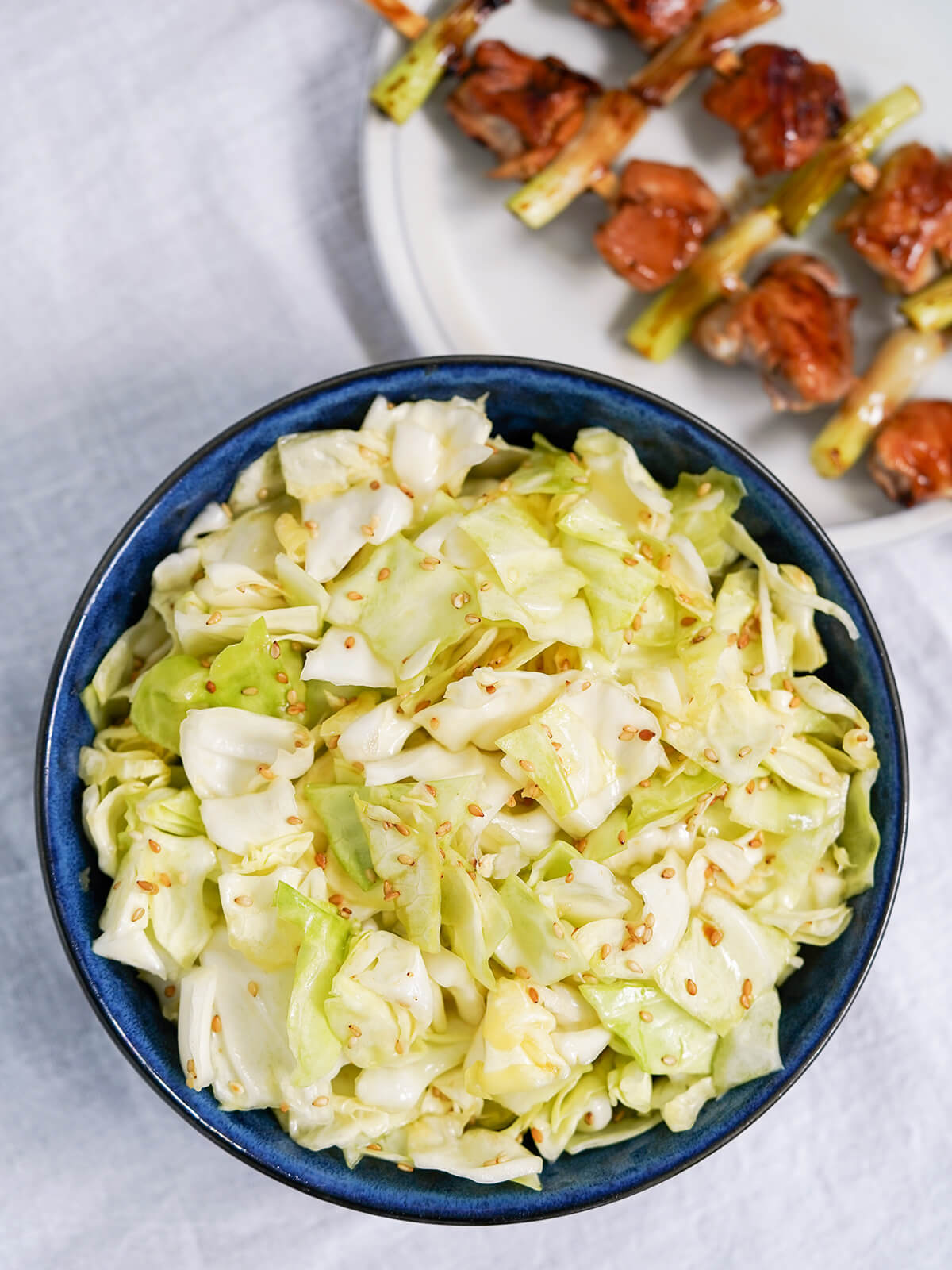 overhead view of bowl of Japanese cabbage salad (yamitsuki cabbage) with chicken yakitori skewers on plate in corner.