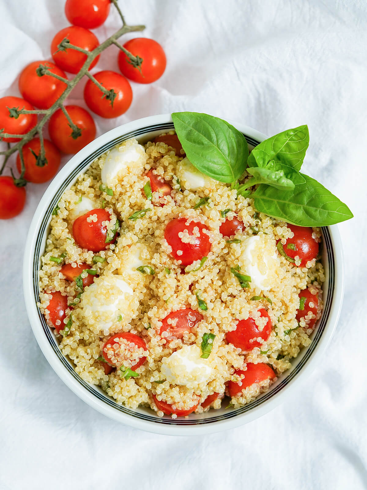 overhead view of bowl of caprese quinoa salad with cherry tomatoes on vine above one corner.