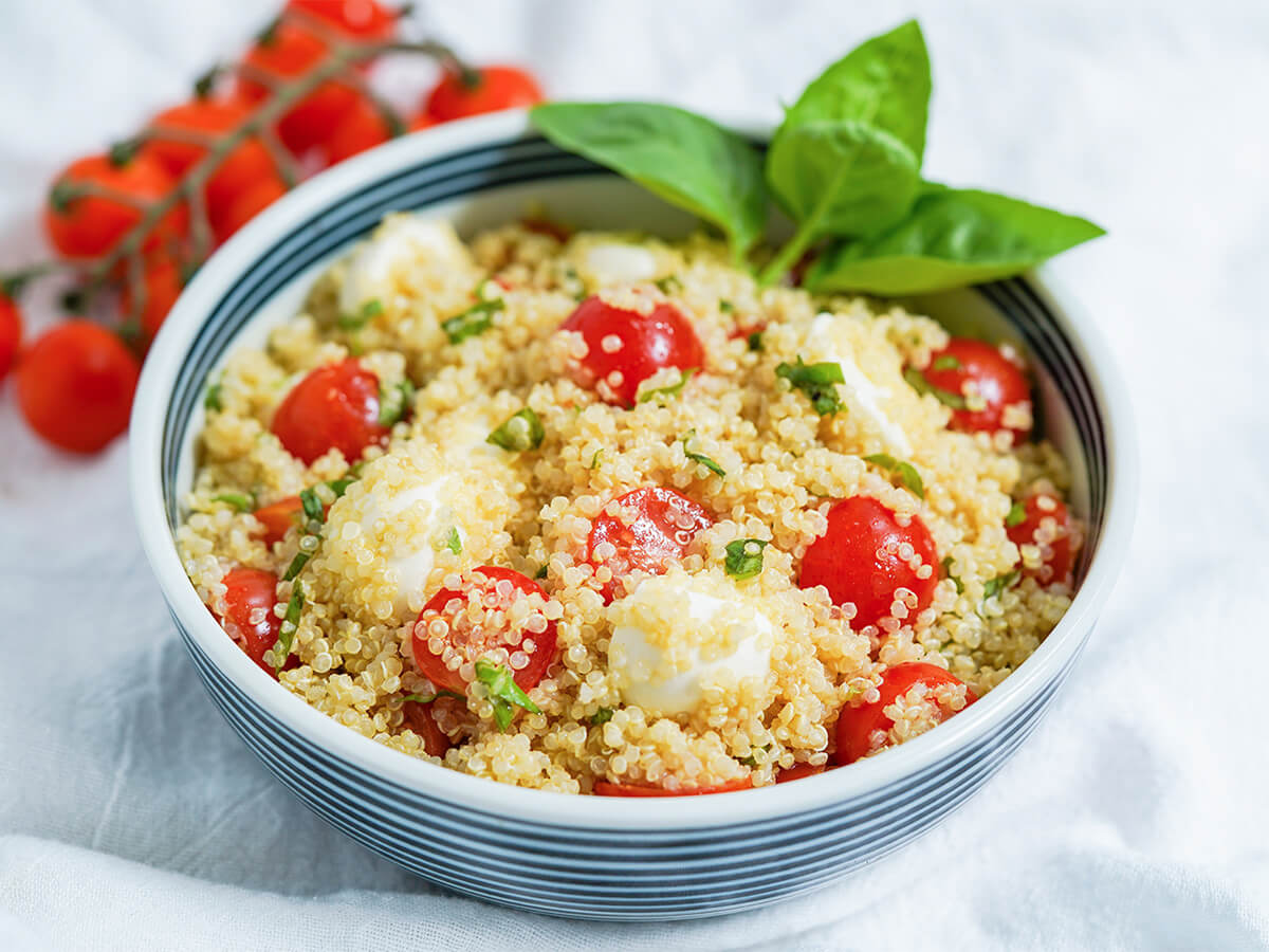 side view of bowl of caprese quinoa salad with stem of tomatoes in background.