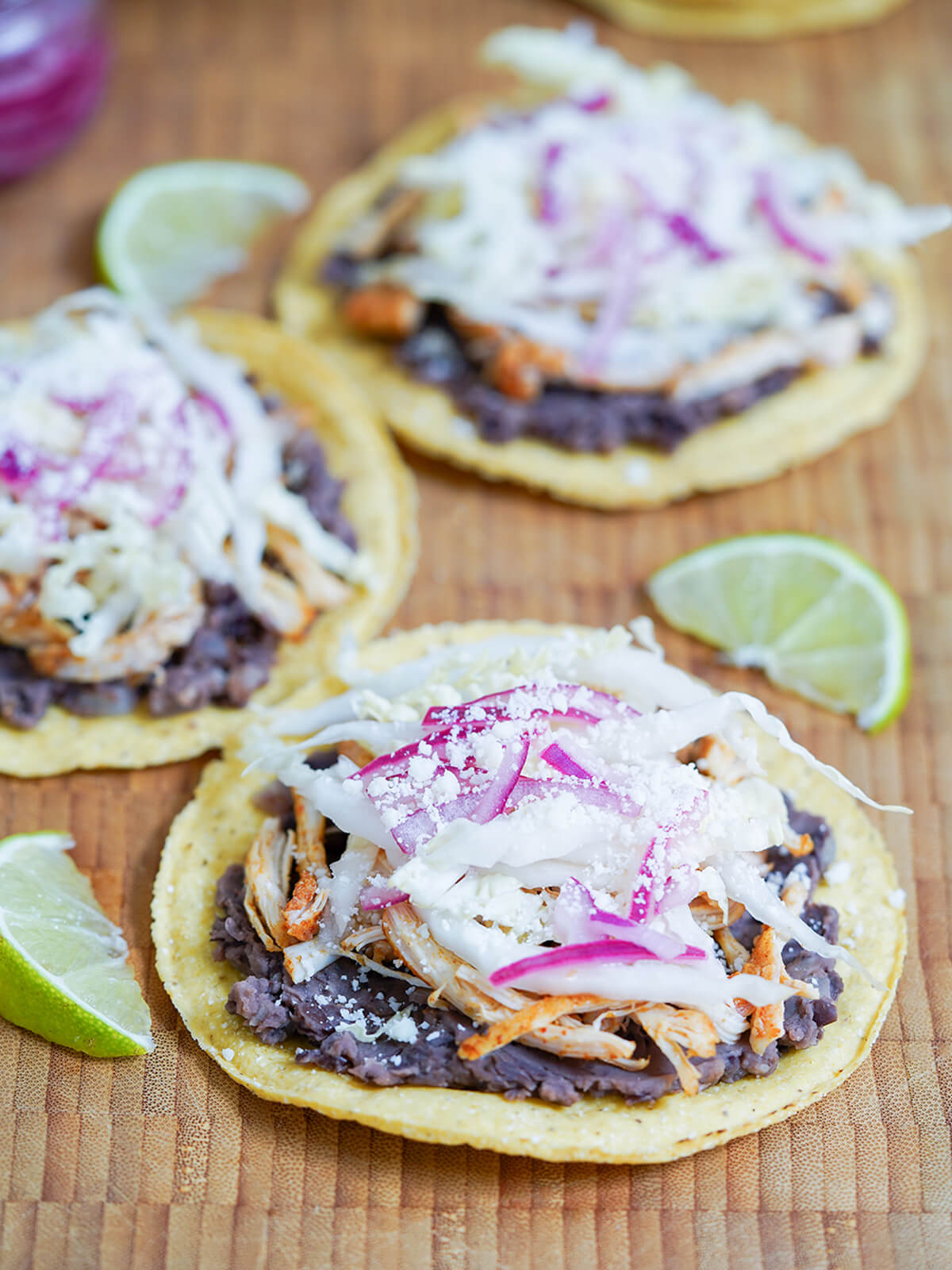 chicken tostadas on wooden board with lime wedges around them.