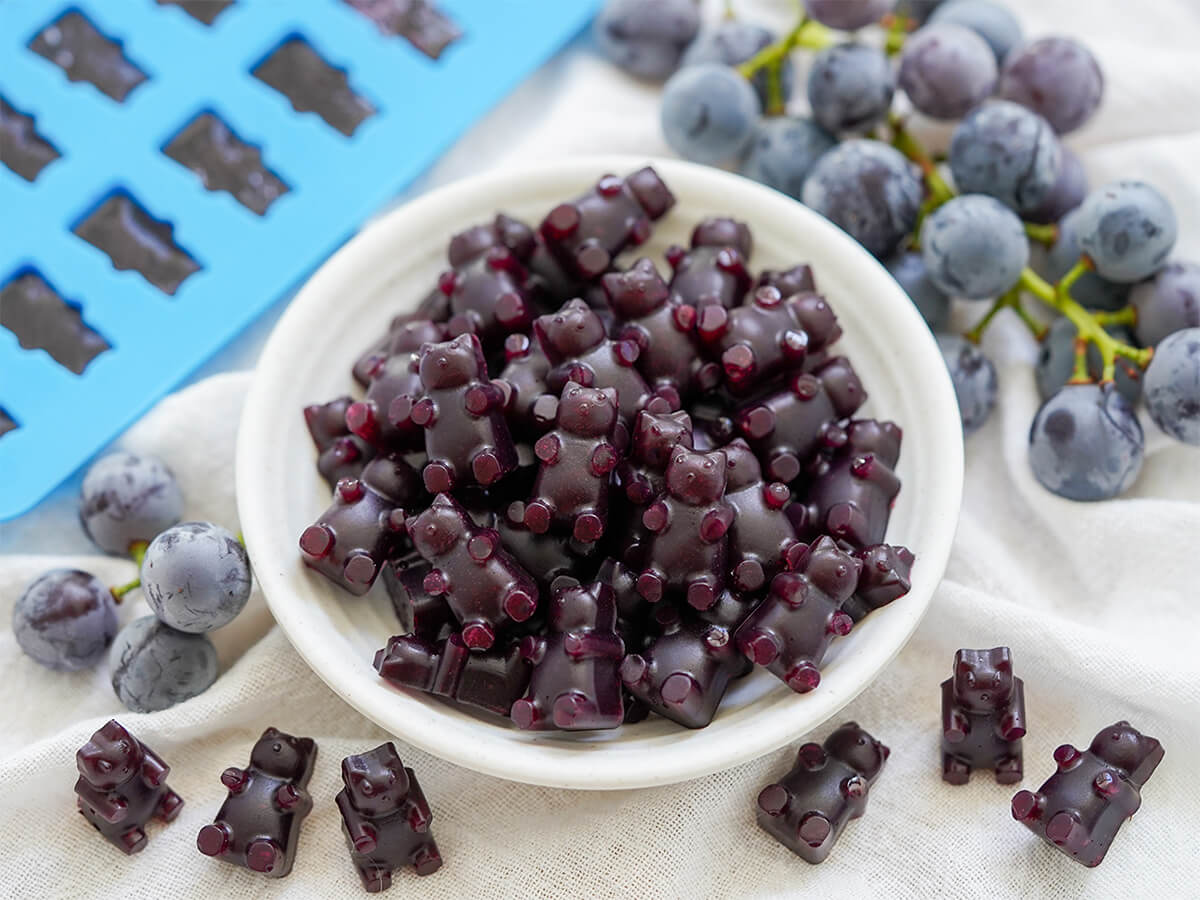 homemade grape gummy bears dish of grape gummy bears with a few in front, grapes either side and some still in mould in corner.