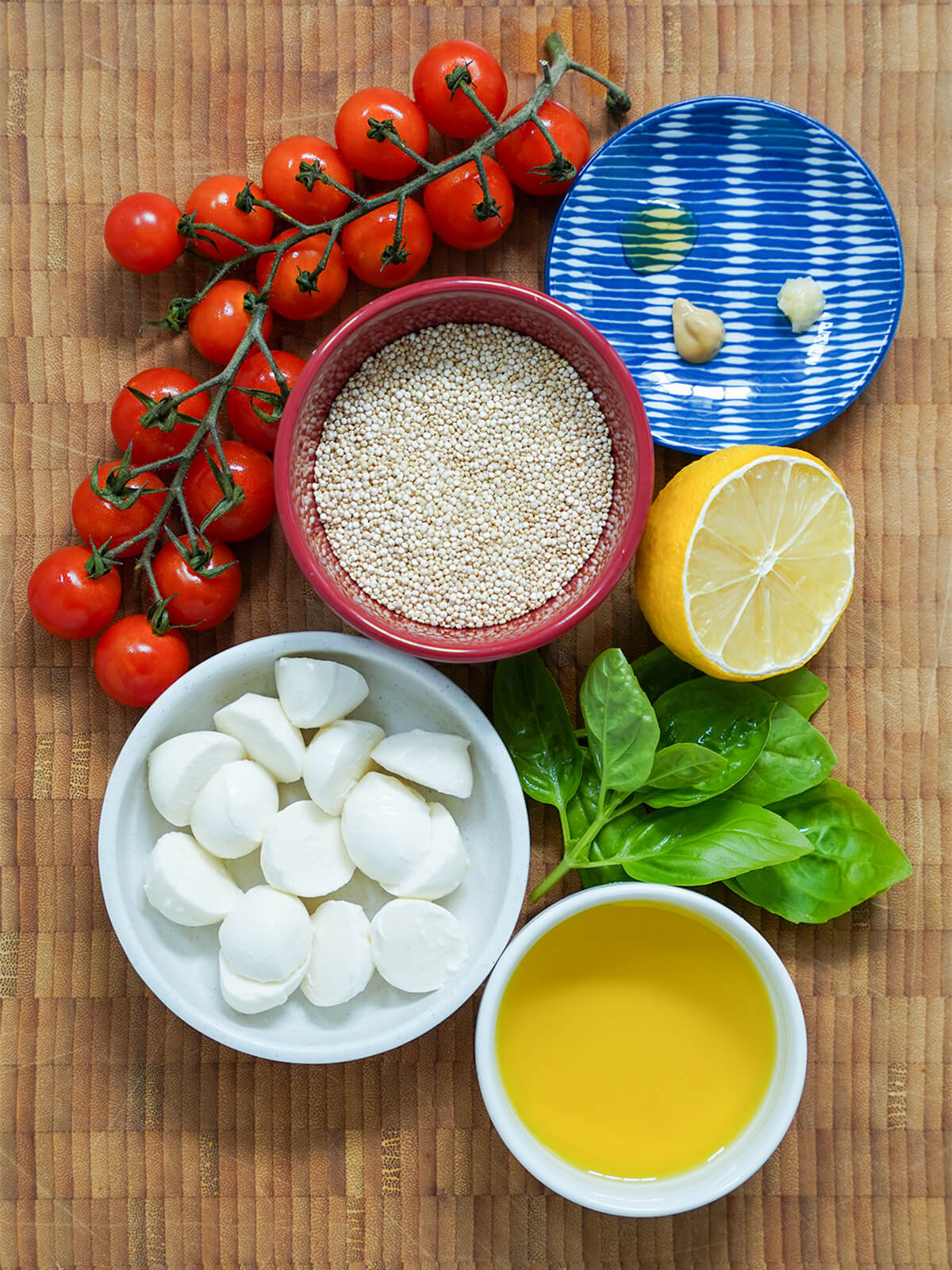 bowls with quinoa, mozzarella, olive oil with part lemon, bunch of basil and cherry tomatoes on vine around.