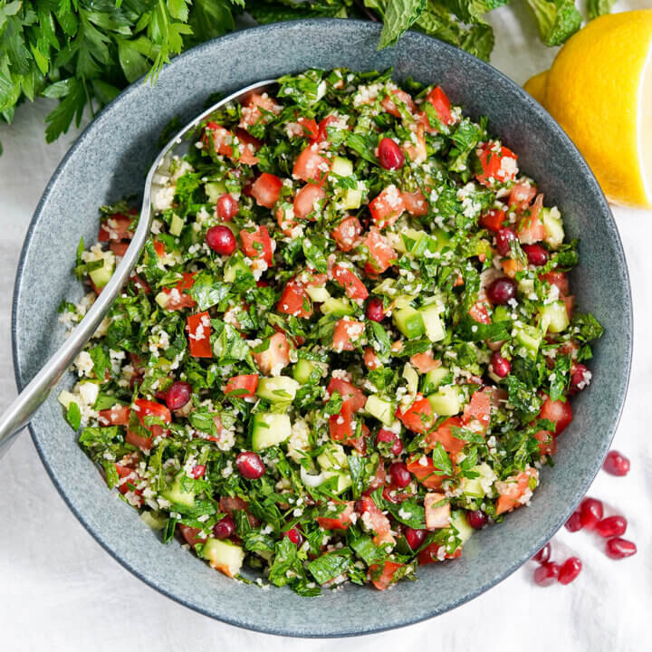 overhead view of bowl of tabbouleh with pomegranate with spoon in bowl to one side.