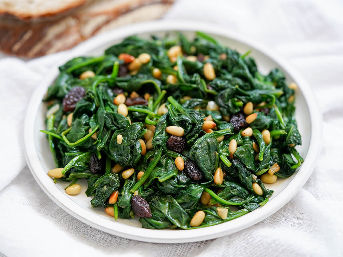 plate of Catalan spinach with pine nuts and raisins close up view of plate of Catalan spinach with pine nuts and raisins.