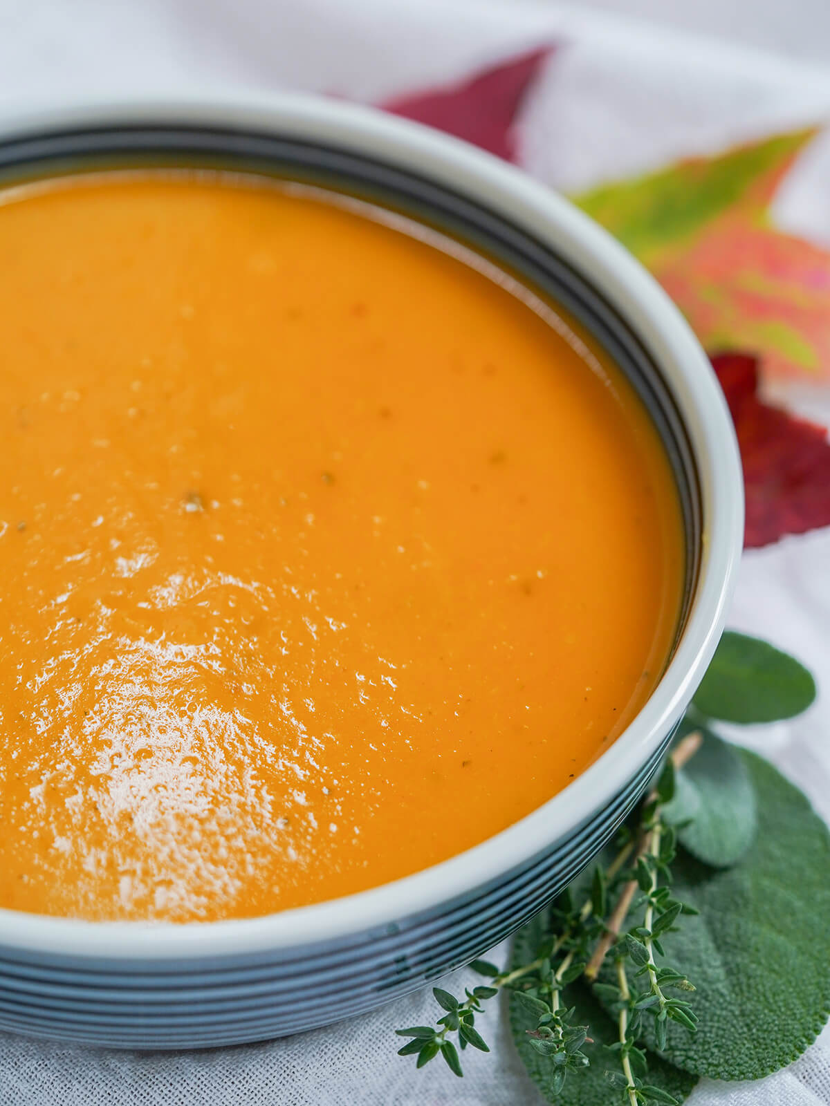 side partial view of bowl of butternut squash apple soup with herbs to side of bowl.