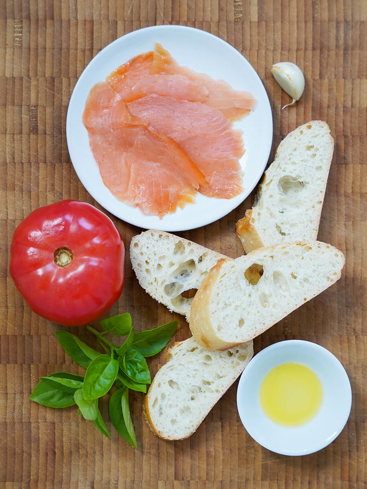 ingredients smoked salmon bruschetta slices of bread, sprigs of basil, tomato and plate with slices of smoked salmon on board.