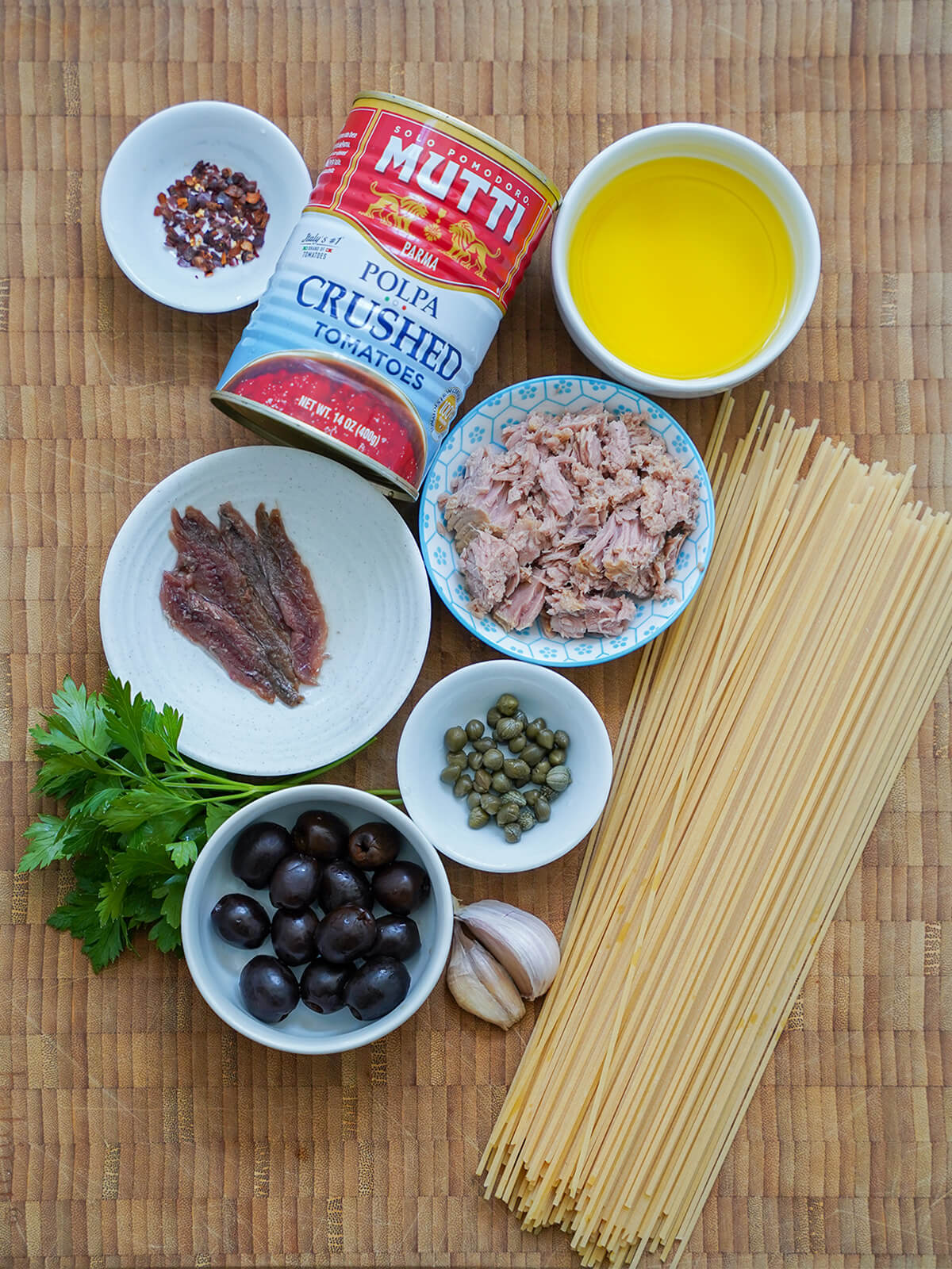 can of tomatoes, spaghetti with dishes of oil, tuna, anchovies, capers, olives and red pepper flakes in between and some garlic and parsley to side.