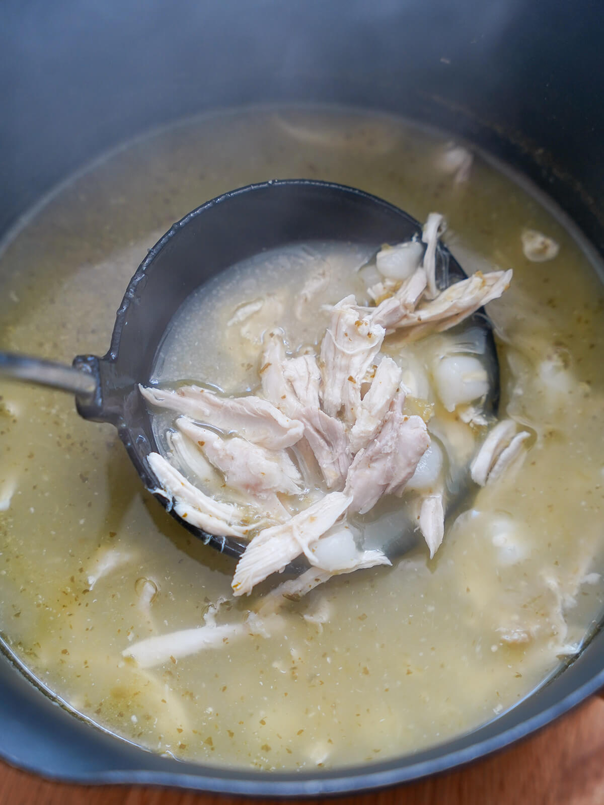ladle taking spoonful from pot of soup with pieces of chicken and hominy in broth.