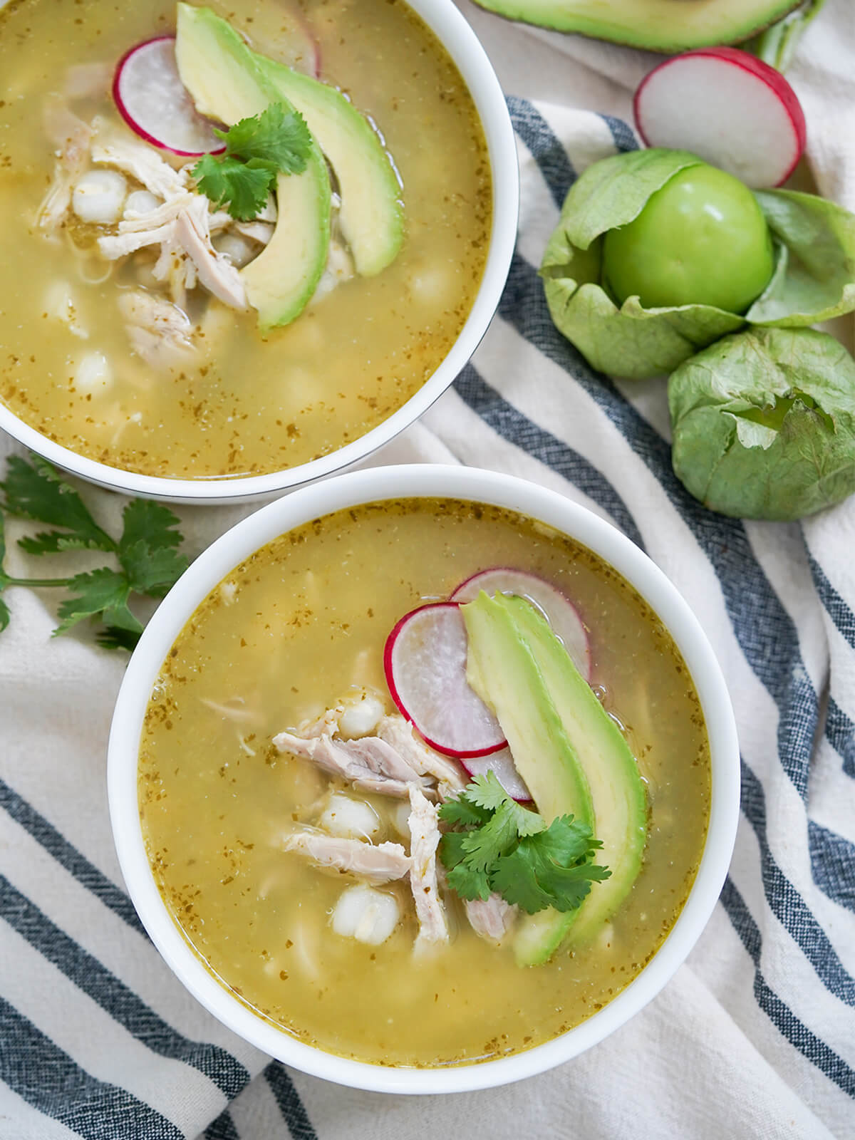 overhead view of two bowls of pozole verde with tomatillo and part radish to one side.