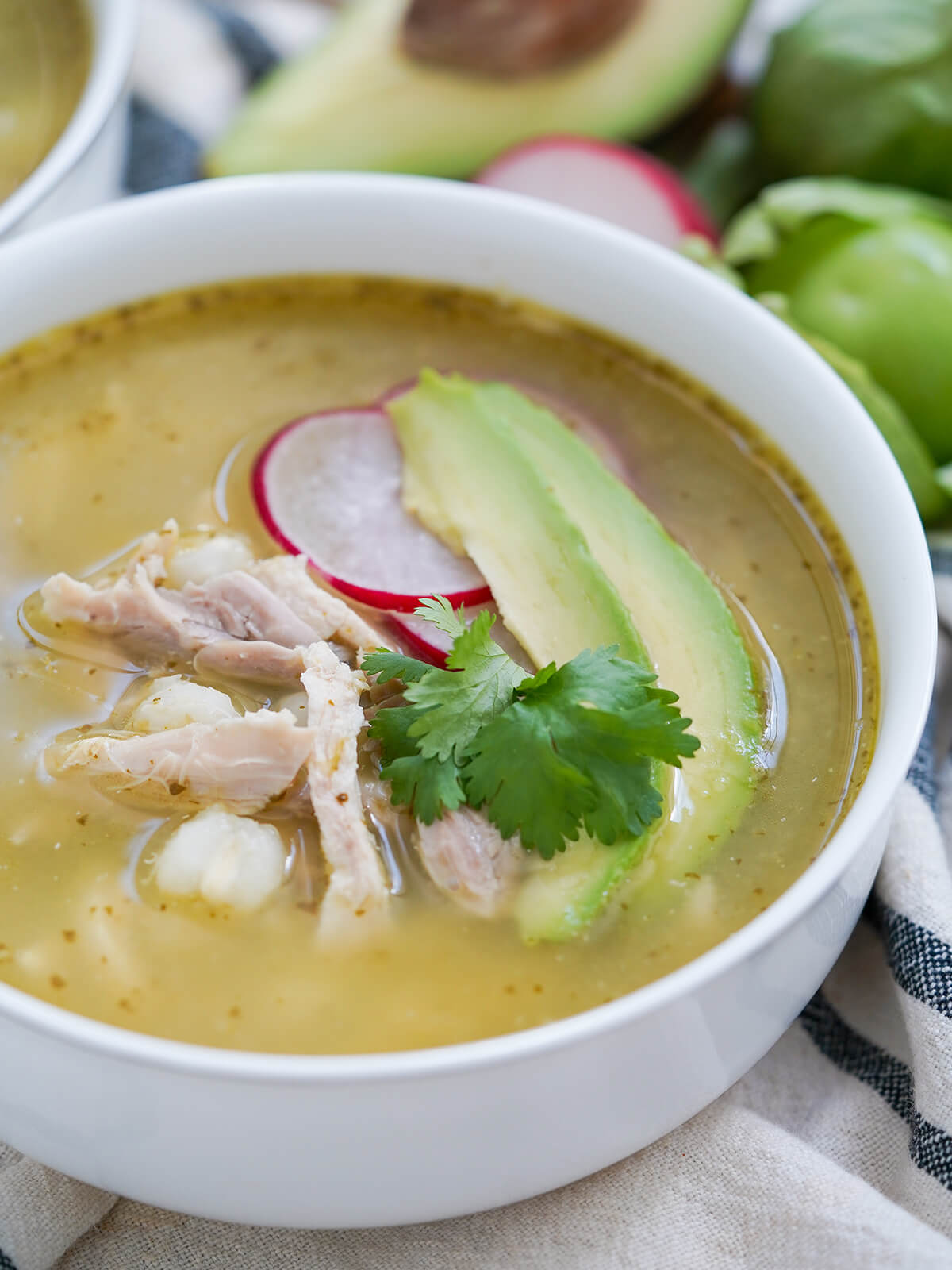 side view of bowl of pozole verde garnished with radish and avocado slices.