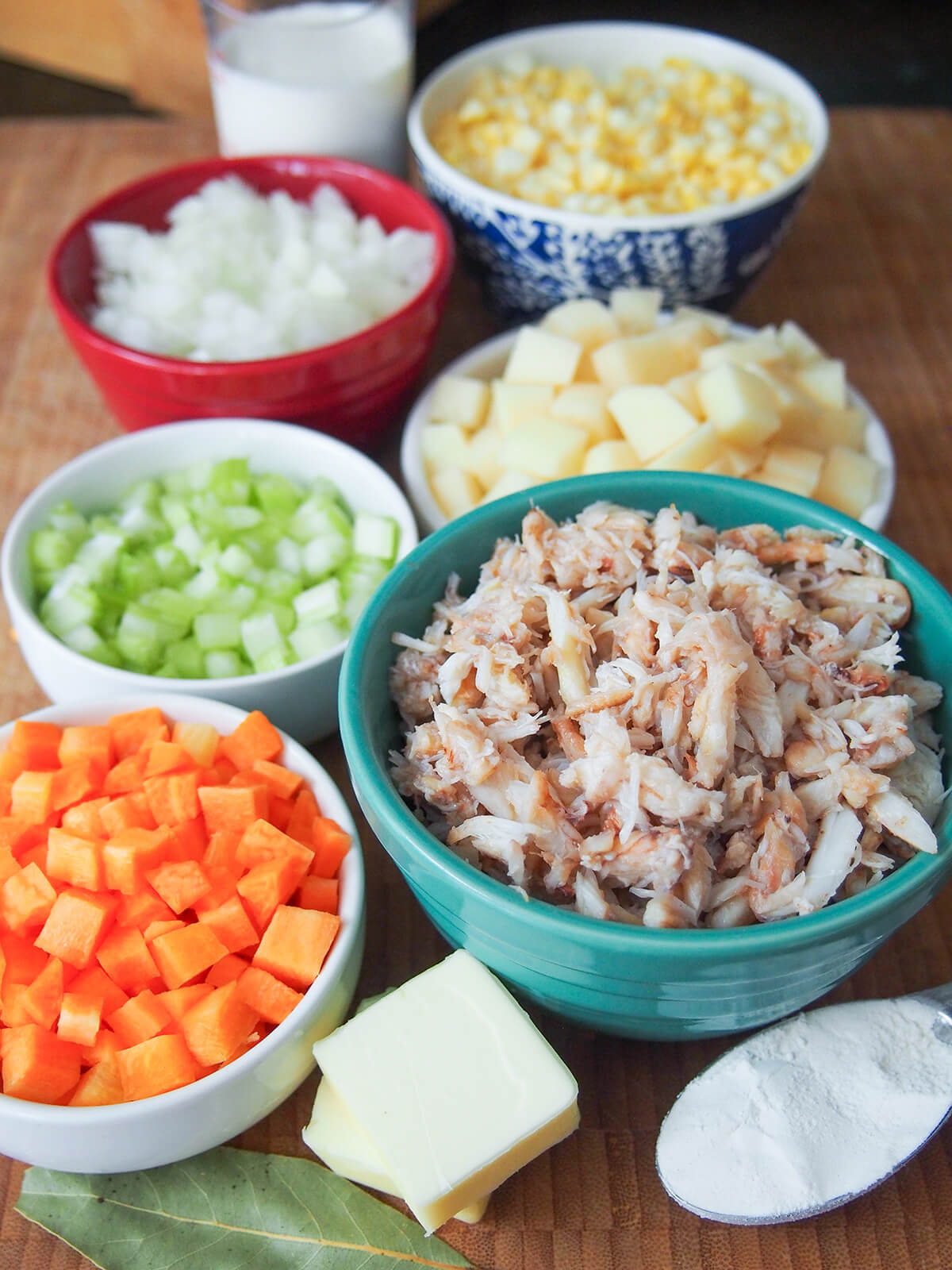 prepared ingredients for crab and corn chowder bowls of diced vegetables and crab with cream behind and chunks of butter and spoon of flour in front.
