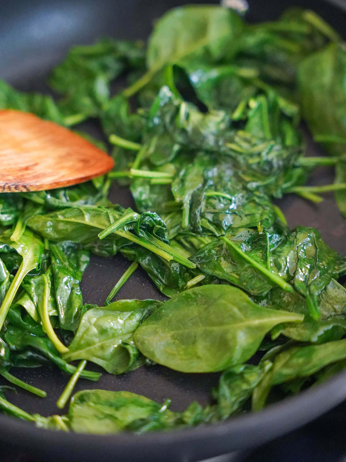 cooking spinach for Catalan spinach with pine nuts and raisins wilting down spinach ni skillet.