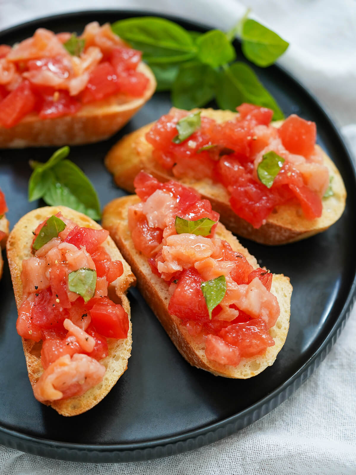 A light and delicious appetizer, this smoked salmon bruschetta is a simple twist on a classic. It's great for any occasion and quick to prepare. pieces of smoked salmon bruschetta on plate with basil in background.