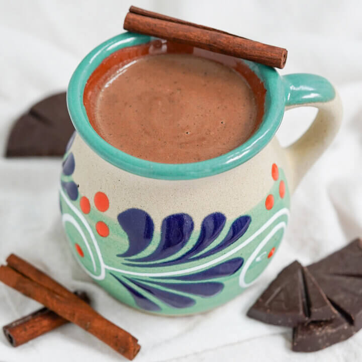 mug of champurrado with cinnamon stick balanced on top.