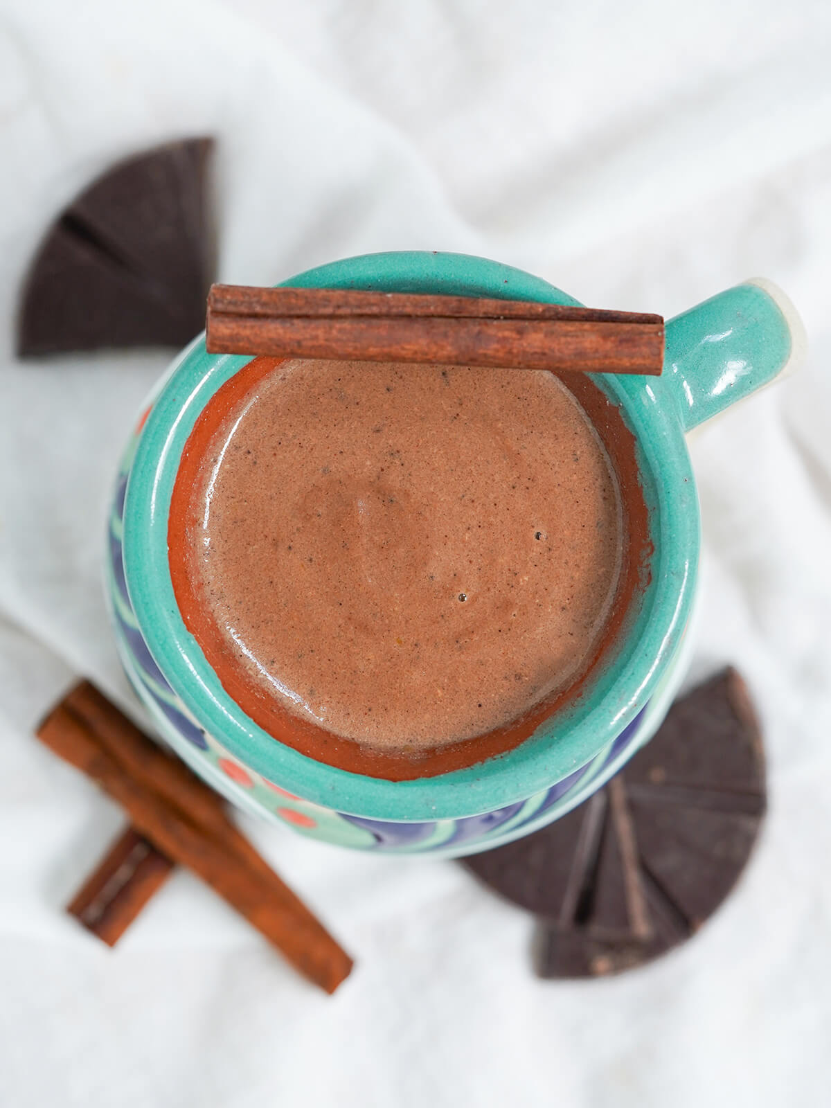 overhead view of mug of champurrado with cinnamon stick resting on rim.