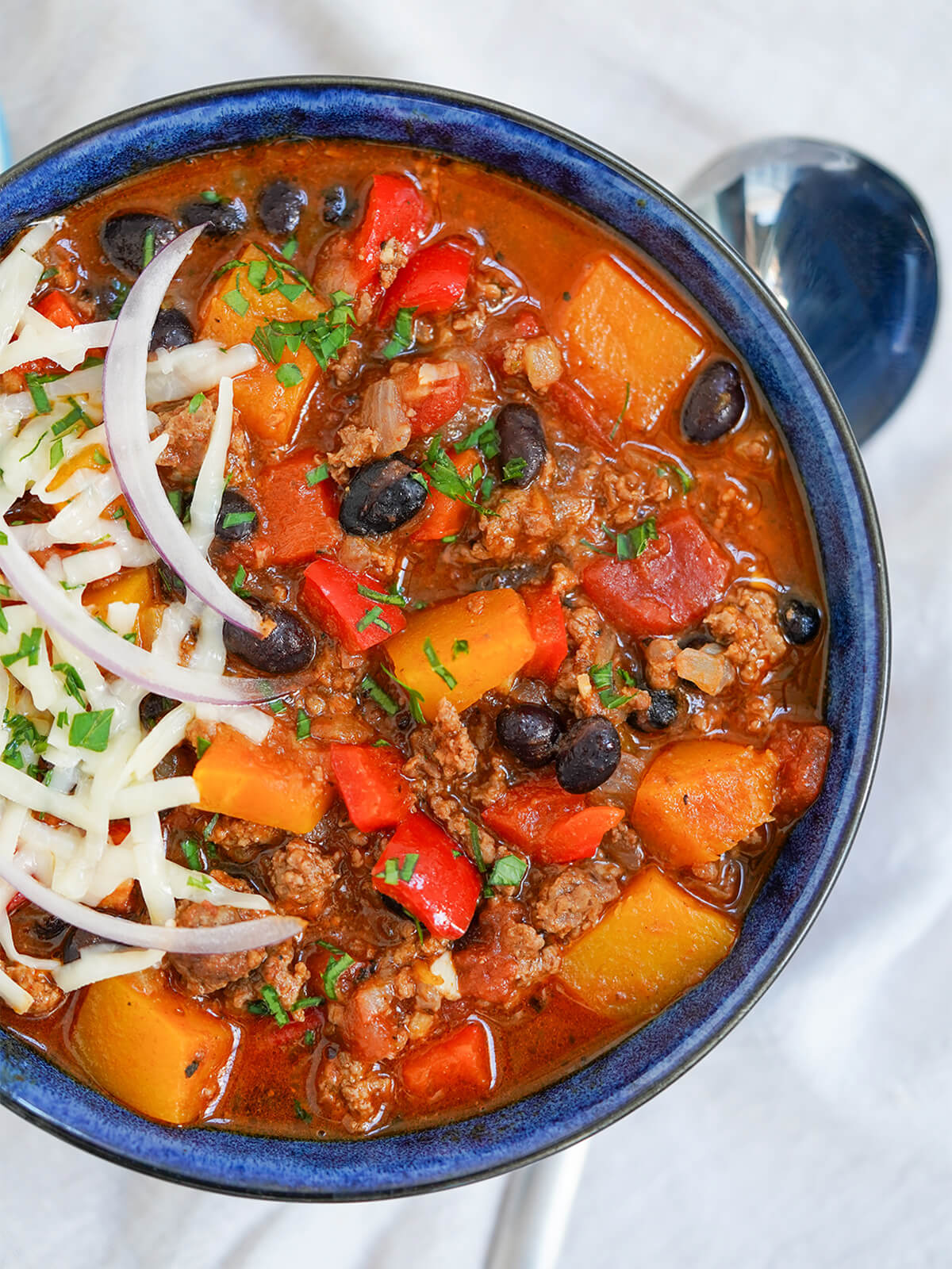 overhead partial view of bowl of chili with butternut squash with spoon under bowl.