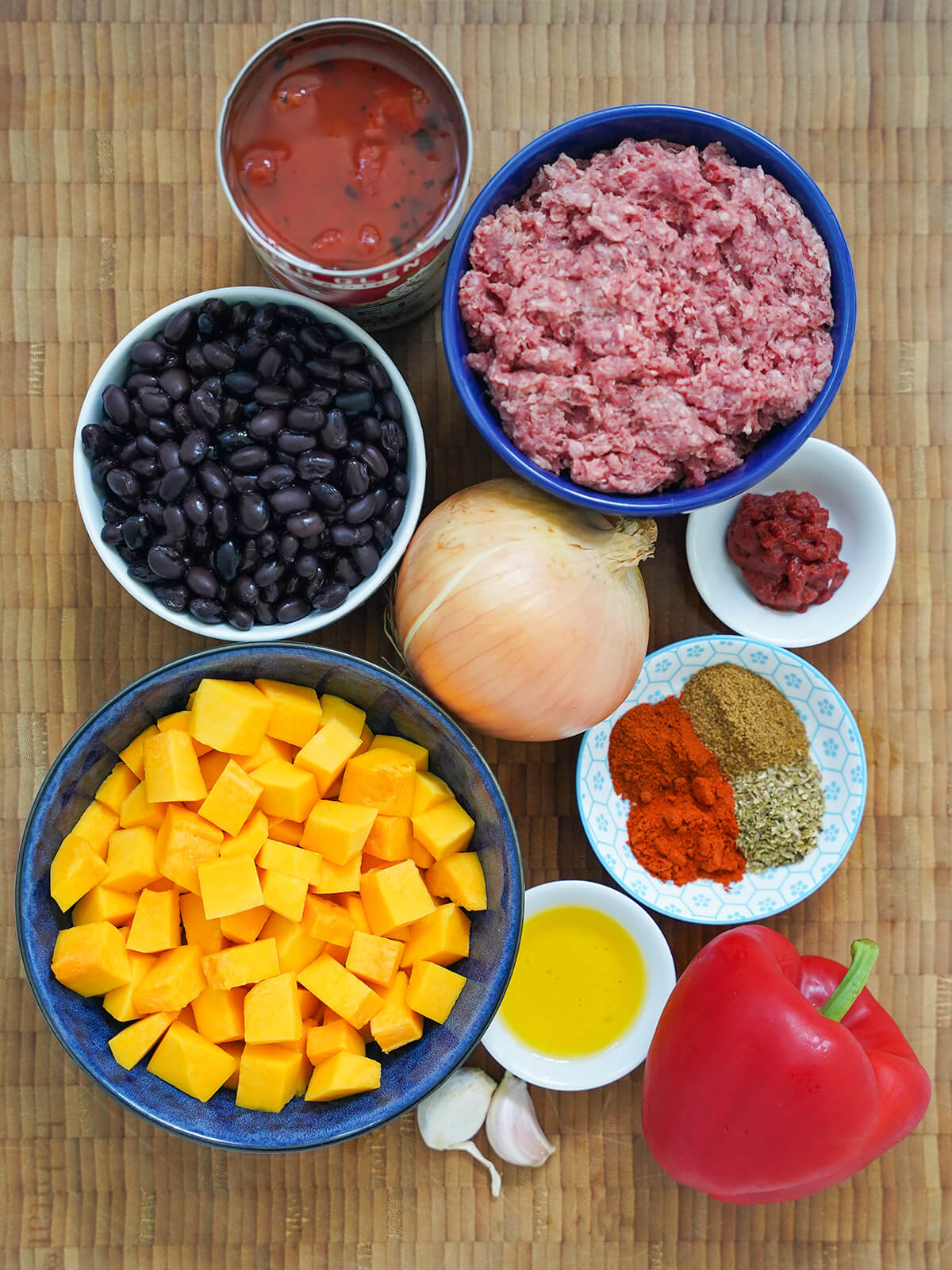 bowls of ground beef, black beans, diced squash, can of tomatoes, onion, pepper, dish with spices.