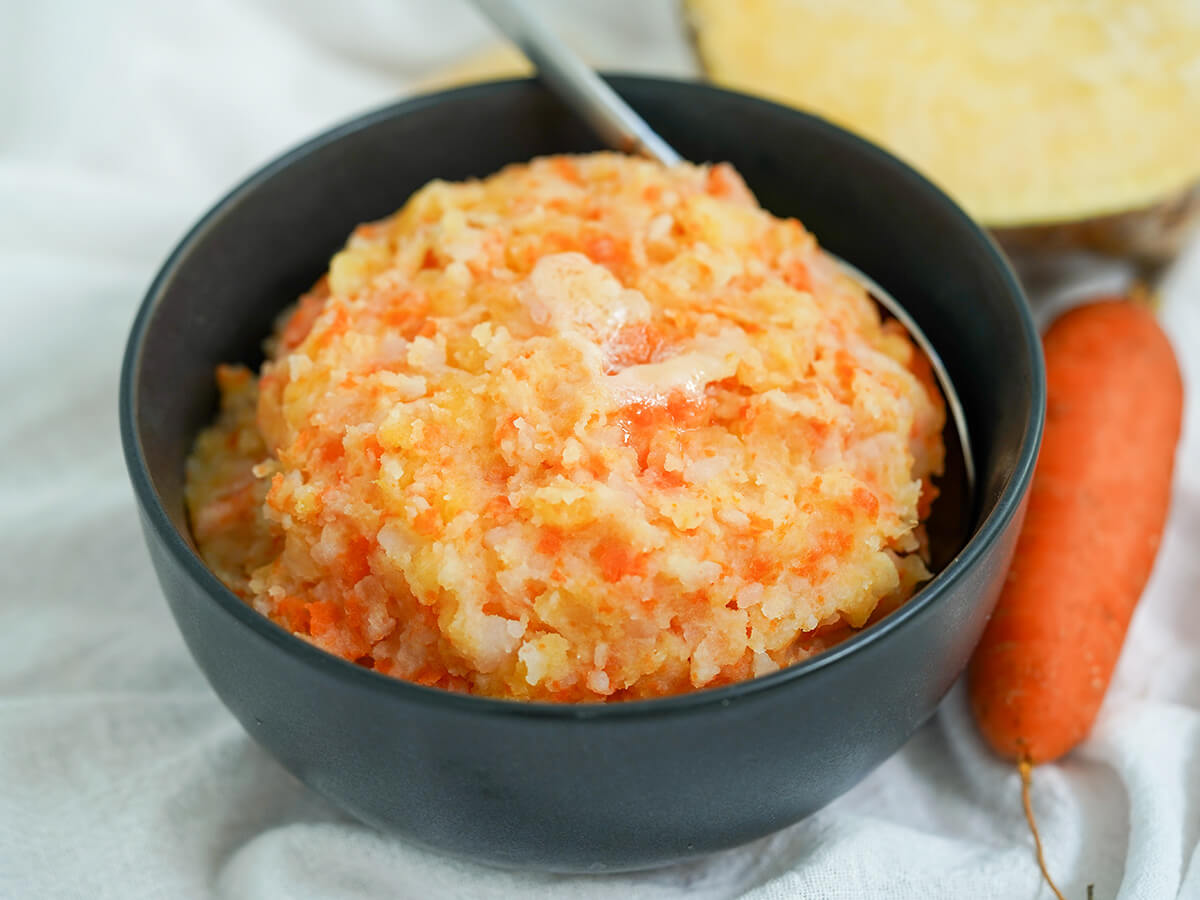 bowl of rotmos, Swedish root vegetable mash with carrot to side.