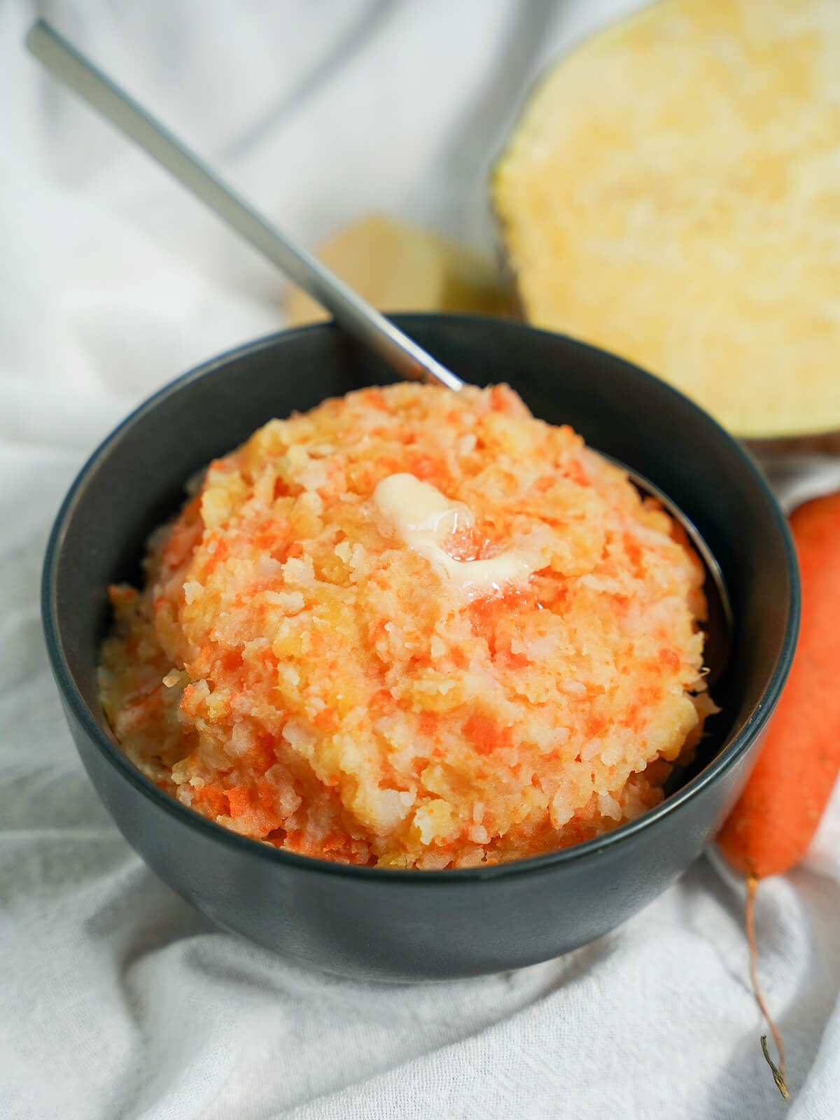 bowl of Swedish root vegetable mash (rotmos) with a spoon sitting in back of bowl.
