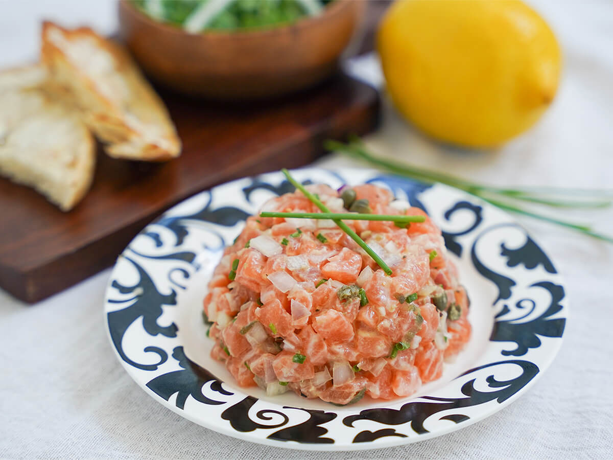 plate of salmon tartare garnished with chives with toast, lemon blurred in background.