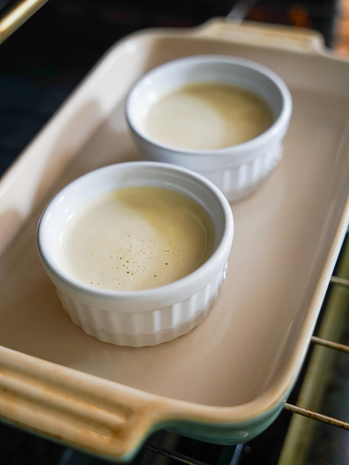 dishes of custard mixture in a baking dish with water. dishes filled with custard mixture in baking dish with water sitting on oven shelf.