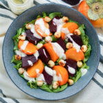 close view of bowl of beet persimmon salad drizzled with goat cheese dressing from overhead.