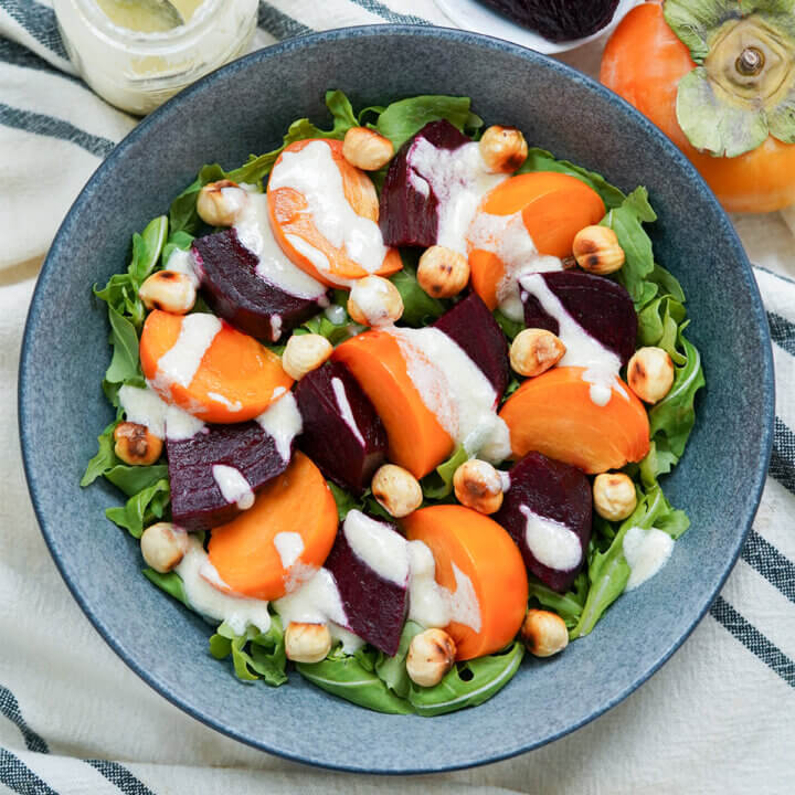 close view of bowl of beet persimmon salad drizzled with goat cheese dressing from overhead.