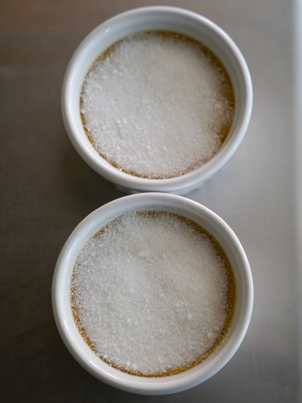 dishes of coffee creme brulee topped with sugar before caramelizing two dishes topped with sugar.