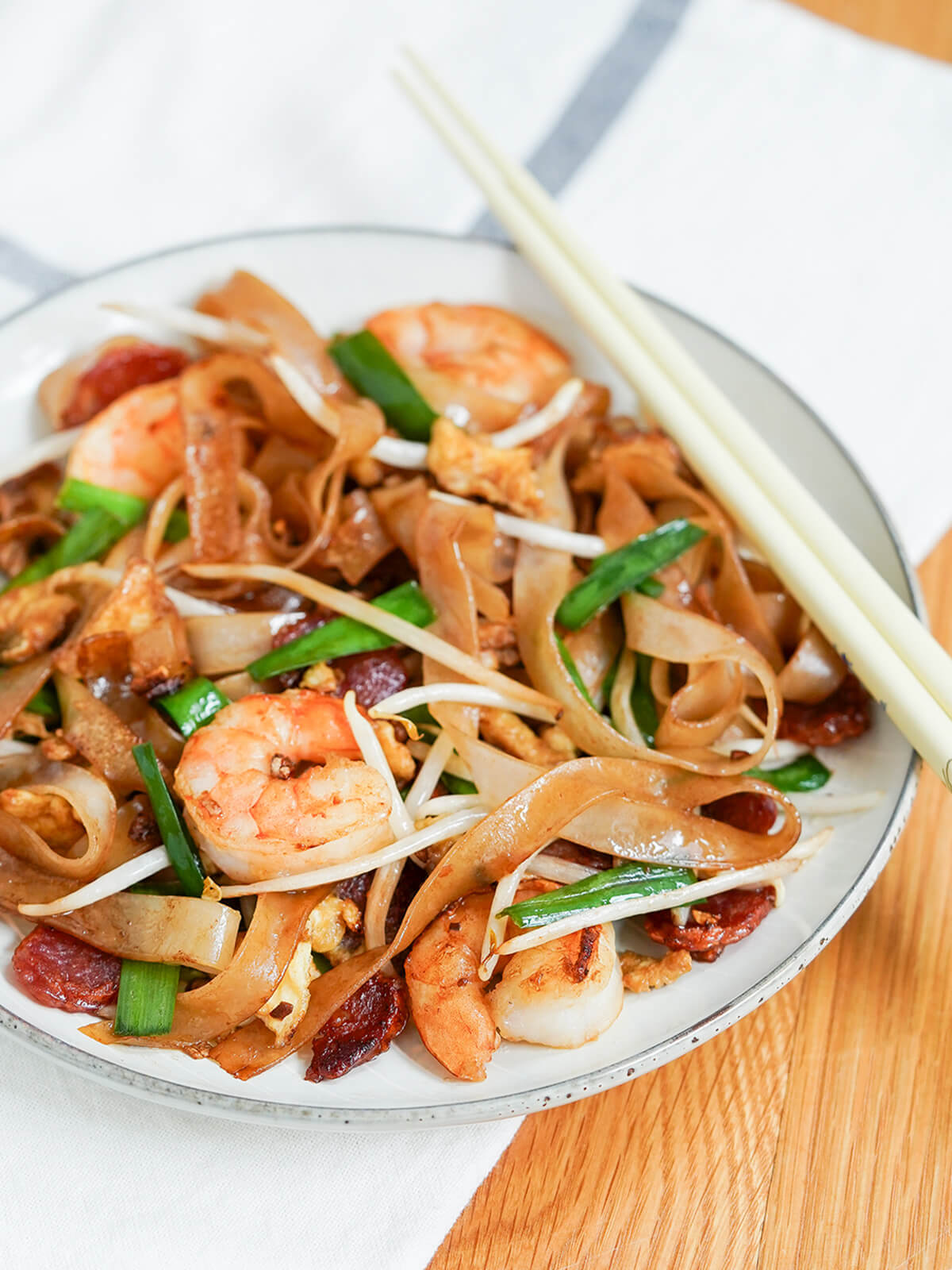 side view of plate of char kway teow with chopsticks on side of plate.