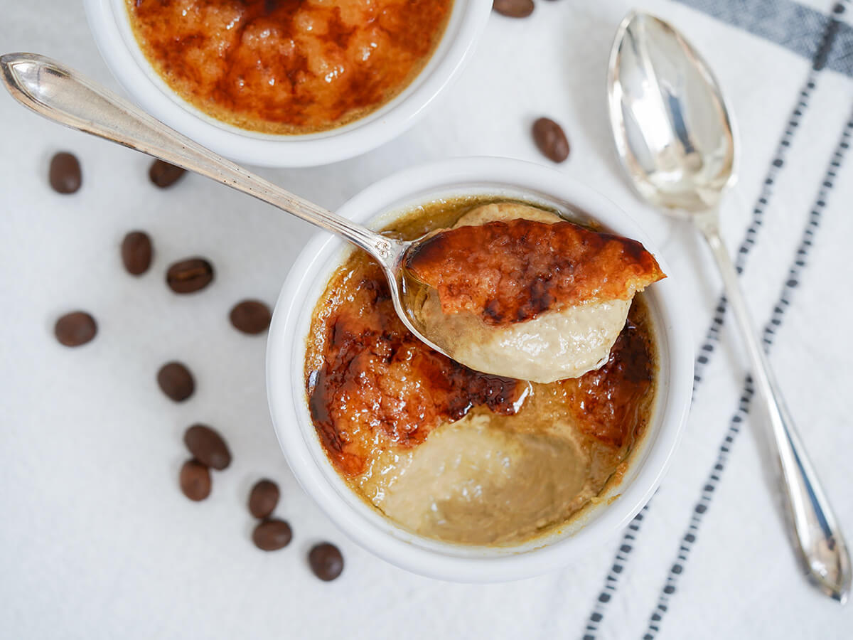 coffee creme brulee overhead view of a spoonful of coffee creme brulee sitting on top of sugar crust of rest in dish.