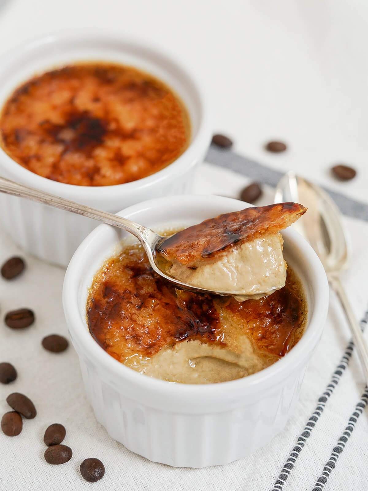spoon of coffee creme brulee sitting on top of rest in dish with another dish behind.