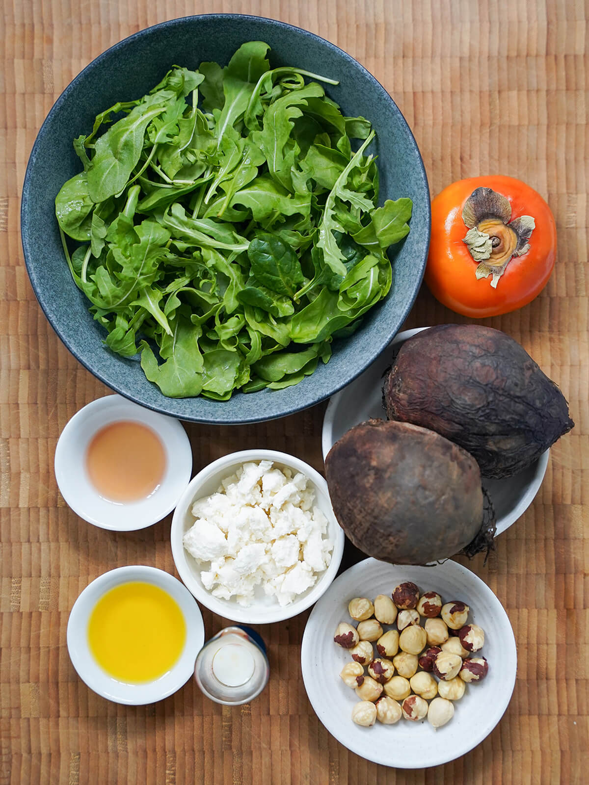 ingredients for beet persimmon salad bowl of greens, a persimmon, some beets, dishes with hazelnuts, goat cheese, oil, milk and vinegar.