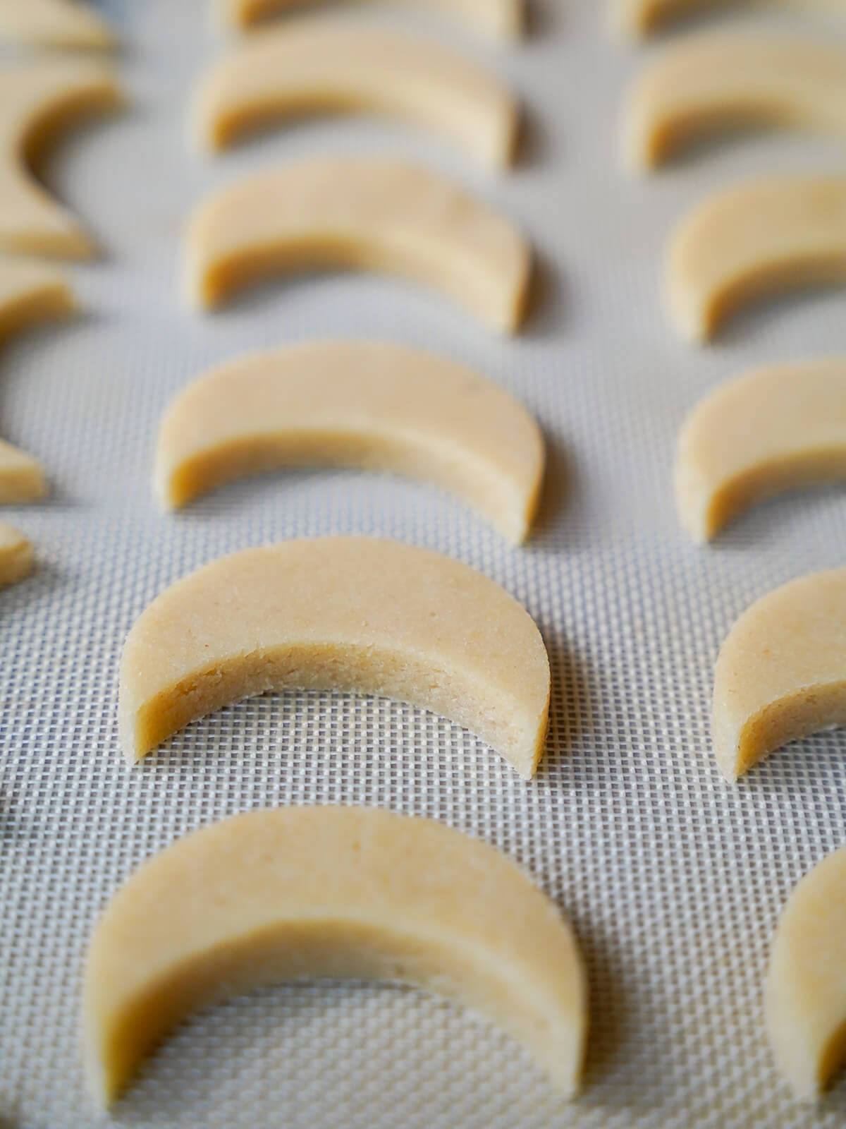 cookies on baking sheet before baking cut out moon shaped cookies on lined baking sheet before baking.