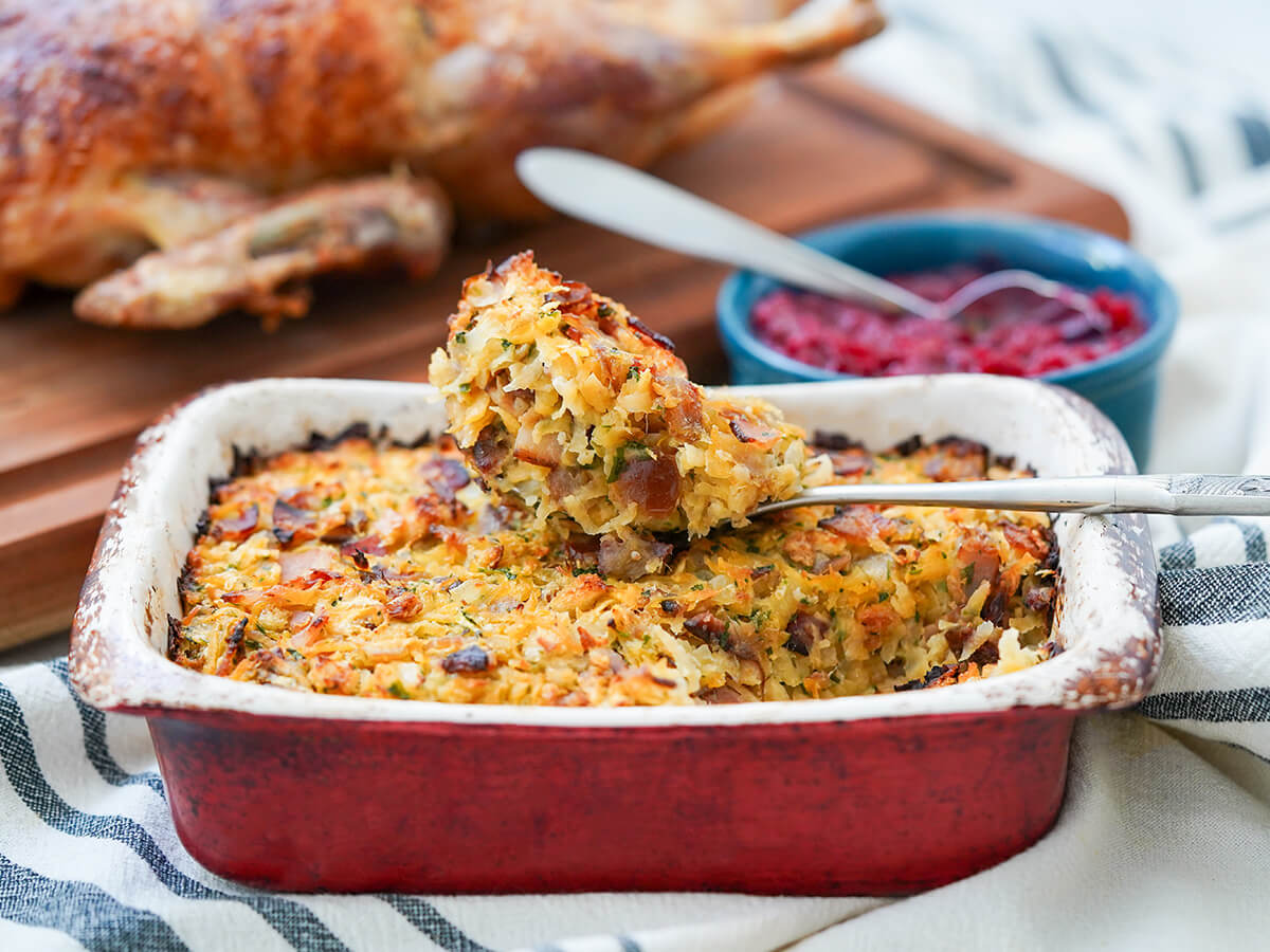 dish of rutabaga date and bacon stuffing with spoonful on top, dish of cranberry sauce and duck blurred behind.