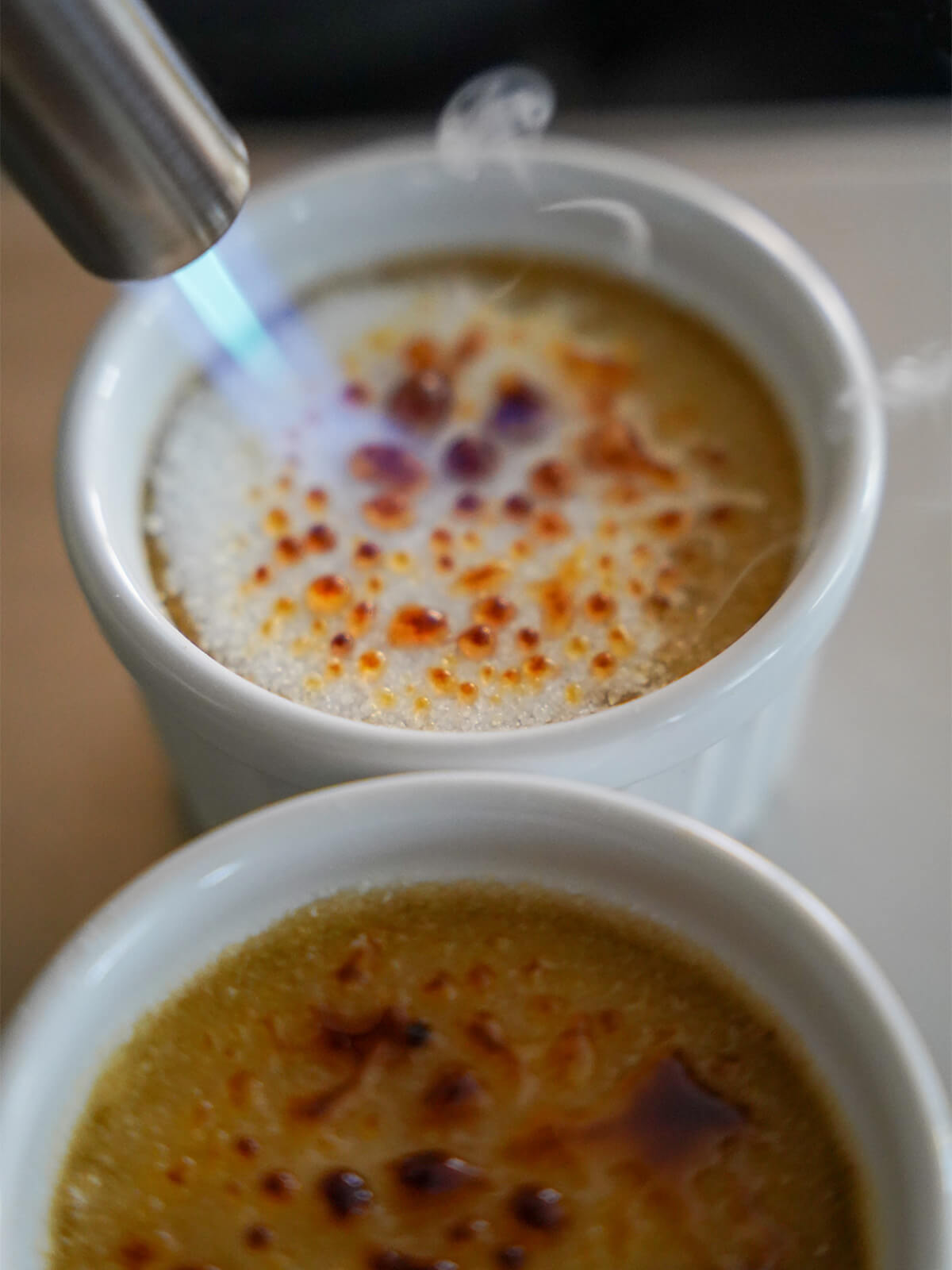 caramelizing sugar on coffee creme brulee using blowtorch on top of coffee creme brulee.