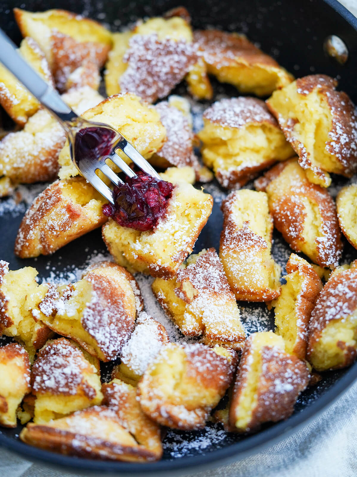 close view of Kaiserschmarrn torn pancakes with fork in a piece of pancake and fruit compote in middle.
