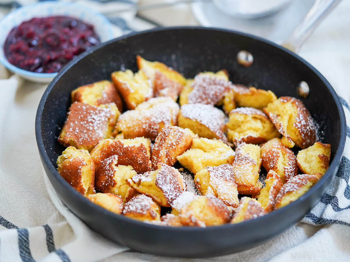 side view of skilletof Kaiserschmarrn torn pancakes with berry compote behind.