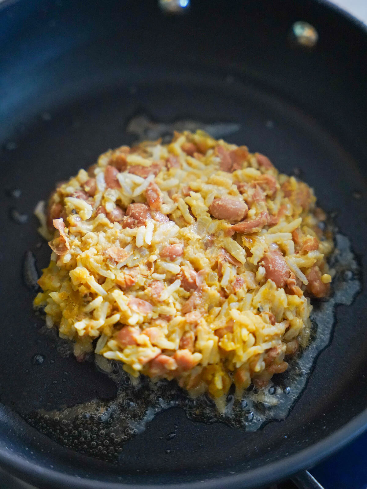cooking tacu tacu "patty" rice and bean mixture formed into a patty frying in oil.
