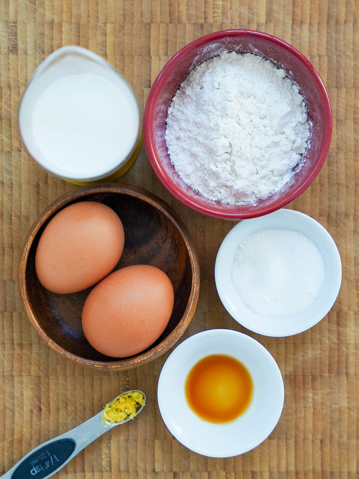 bowls of flour, sugar, milk, eggs with small amounts of vanilla and lemon zest below.